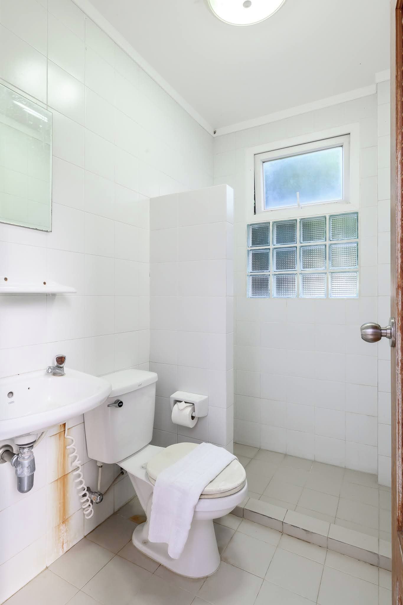 Un baño pequeño y blanco con inodoro, lavamanos y ventana.