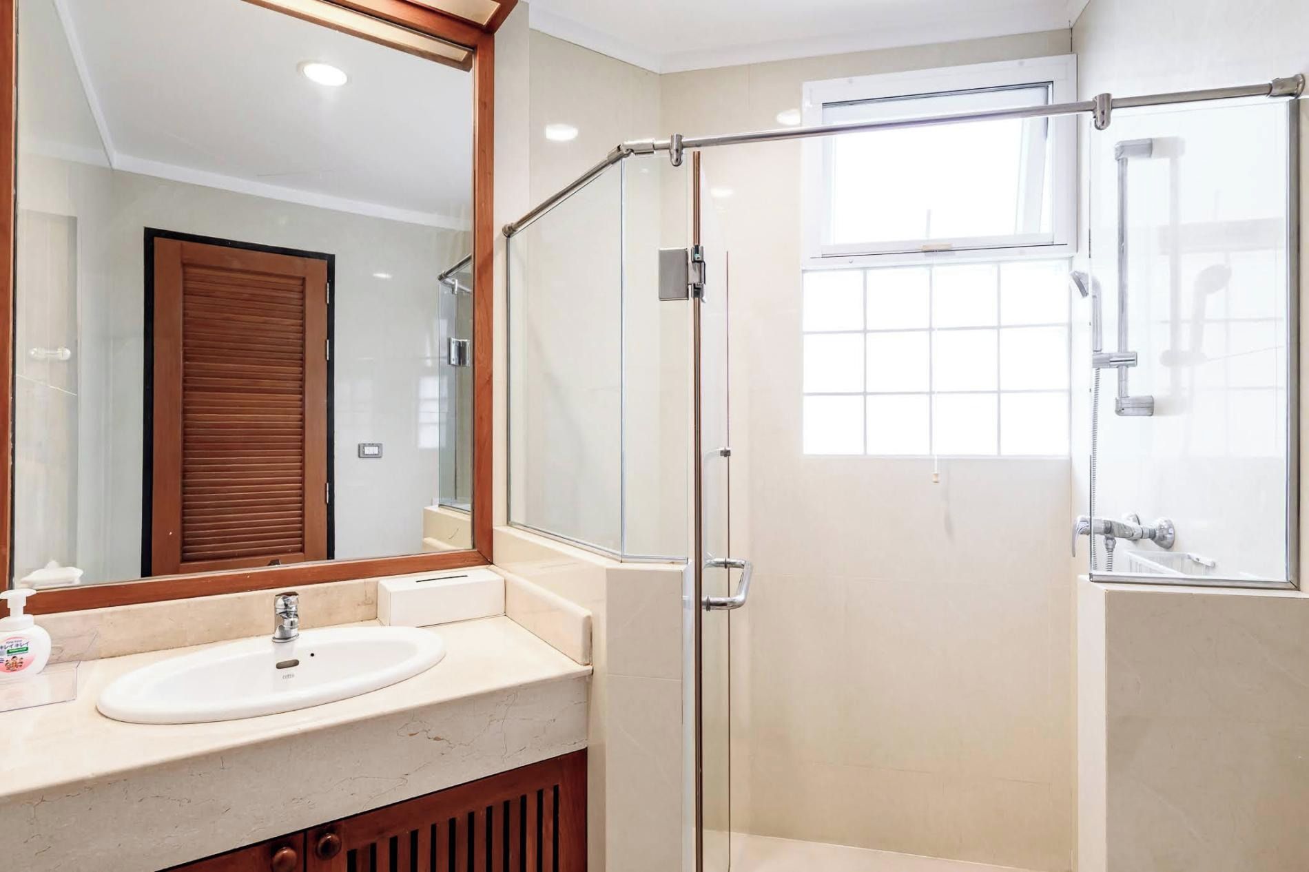Un baño moderno con cabina de ducha de vidrio, lavabo con espejo y ventana que proporciona luz natural.