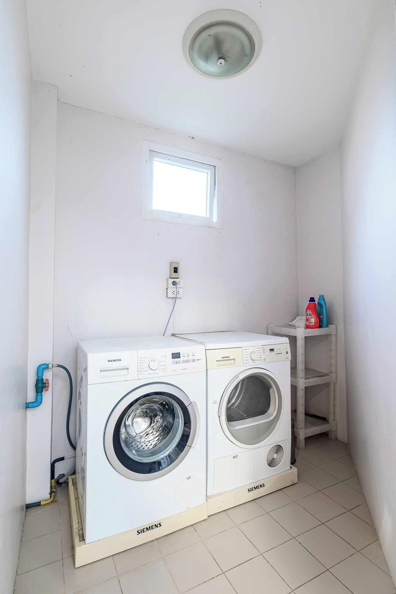A laundry room with two Siemens washing machines, a small window, and a power outlet on the wall.
