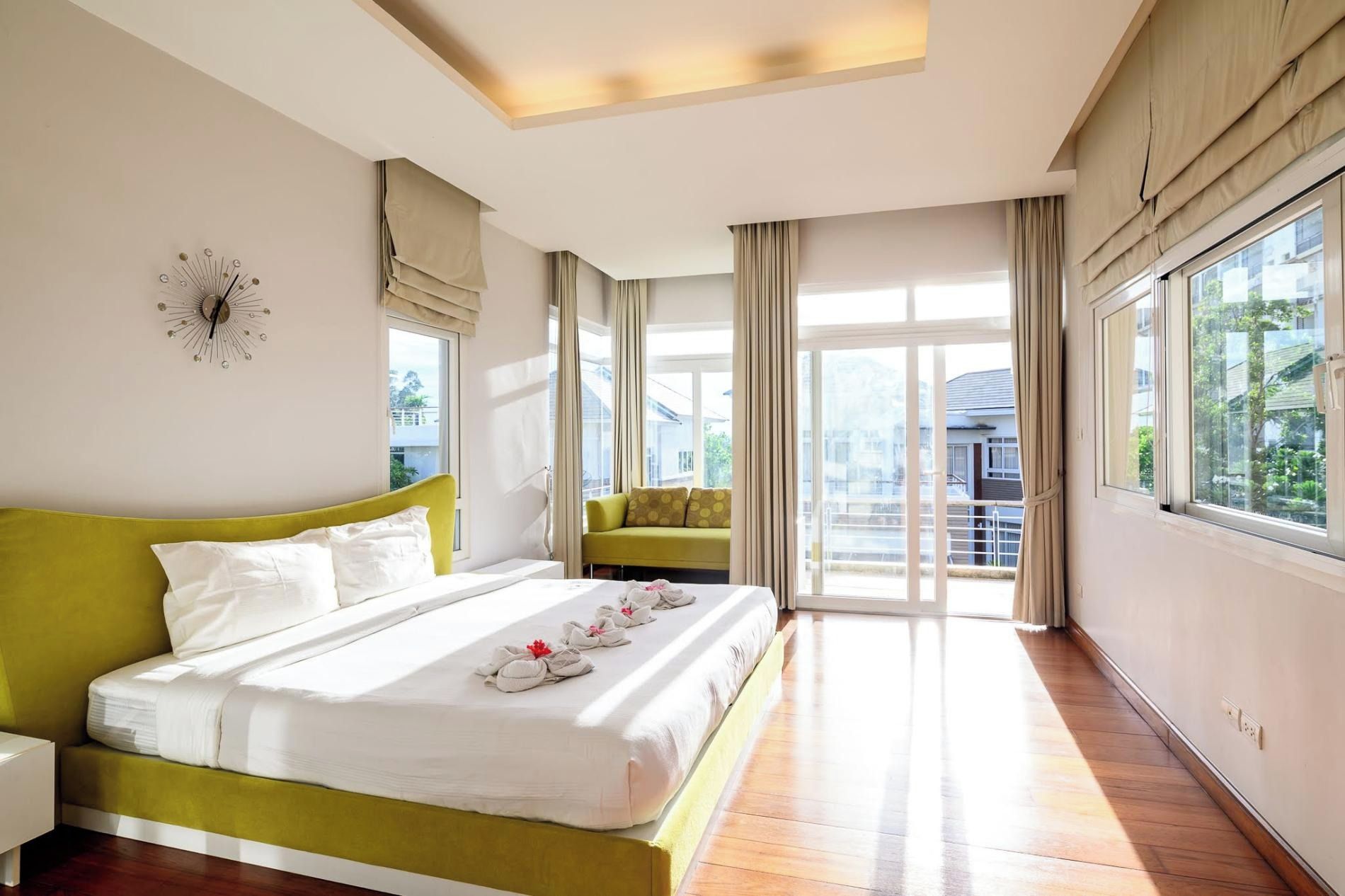 Een hotelkamer met een groot bed, een groene bank, een balkon met gordijnen en uitzicht op de omgeving.