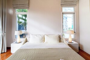 A hotel room with a large bed, two bedside tables with lamps, a view of the outside through two windows, and a white wall. - Modern 2BR Beachside Pool Villa (BA2) (Sattahip)