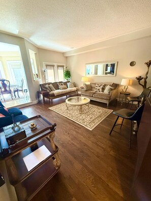 A spacious living room with a large sofa set, a coffee table, and a dining area with a tray table. - Erin Mills Mall • Self Check-in • 2 min to Transit (Mississauga)