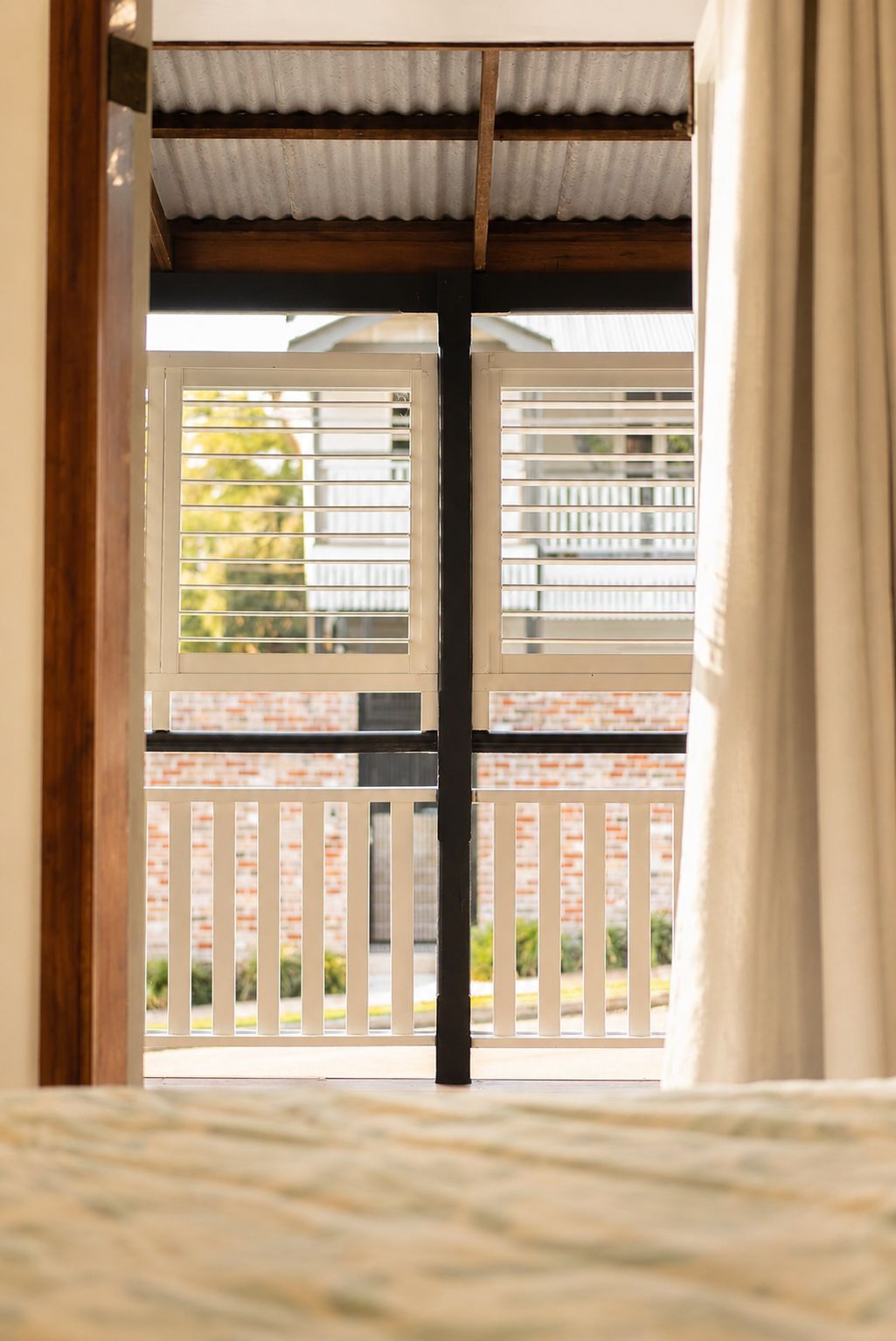 A room with a view through a window with blinds, a wooden floor, and a curtain.