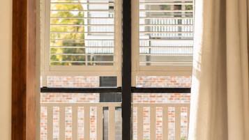 A room with a view through a window with blinds, a wooden floor, and a curtain.