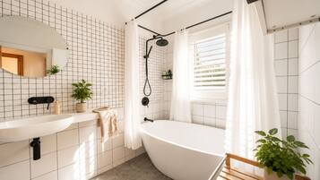 A modern bathroom with a freestanding bathtub, a large mirror, and a window with blinds.