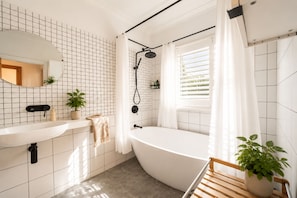 A modern bathroom with a freestanding bathtub, a large mirror, and a window with blinds. - The Sunlit Verandah | Charming Timber Retreat (Annerley)