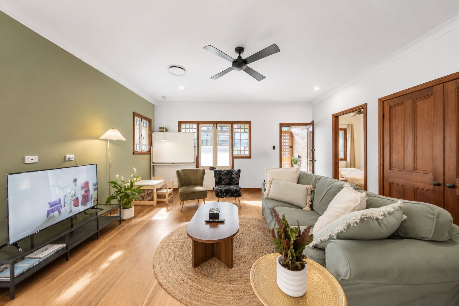 A living room with a flat-screen TV, a ceiling fan, a sofa, a coffee table, and a dining area with a table and chairs.