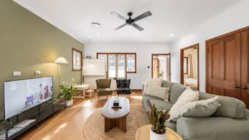 A living room with a flat-screen TV, a ceiling fan, a sofa, a coffee table, and a dining area with a table and chairs.