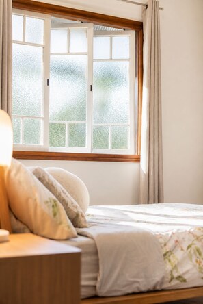 Une chambre à coucher avec un lit, une table de chevet, une lampe et une fenêtre avec des rideaux.