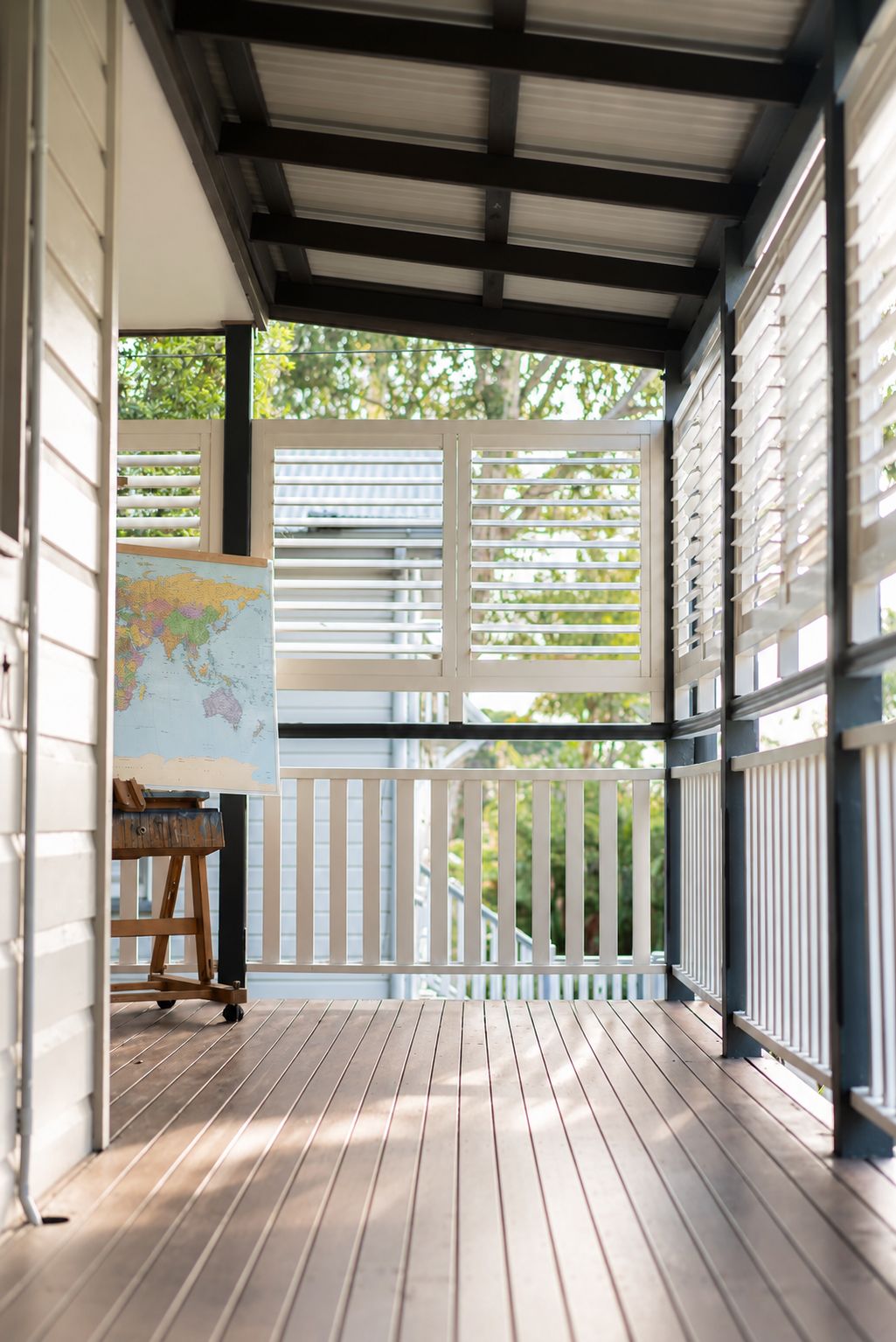 A covered porch with a wooden floor, a white railing, and a map on a stand.