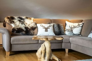 Ein graues Sofa mit einer großen Felldecke, einem runden Couchtisch aus Holz und dekorativen Kissen mit Tiermotiven.
