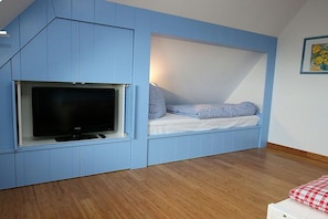 Ein Zimmer mit integriertem Fernseher, einem Bett mit Karomuster-Bettwäsche und Holzboden.