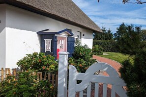 Une maison blanche avec un toit de chaume, une porte bleue et une clôture en bois peinte en blanc.