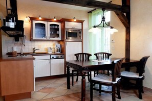 A kitchen with white cabinets, a stove, an oven, and a dining table with chairs. - Holiday apartment with 1 bedroom (Seebad Ahlbeck)
