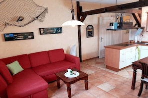 A cozy living area with a red sofa, a wooden coffee table, and a kitchen area with a white countertop and cabinets. - Holiday apartment with 1 bedroom (Seebad Ahlbeck)