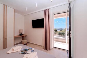 Ein Hotelzimmer mit Bett, Flachbildfernseher, Fenster mit Vorhängen und Blick ins Freie.