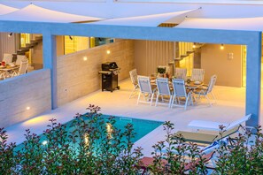 Ein moderner Essbereich im Freien mit Pool, umgeben von einer überdachten Terrasse.