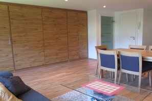 A modern living room with a sofa, a glass coffee table, and a dining table with chairs. There is a wooden wardrobe and a door leading to another room. - Holiday apartment with 2 bedrooms (Rietzlern)