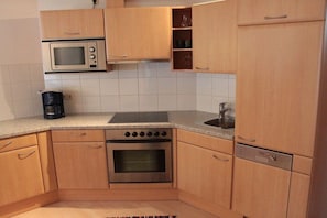 A kitchen with wooden cabinets, a microwave, a stove, and a coffee maker. - Fisherman's dream by the lake (Nesselwängle)