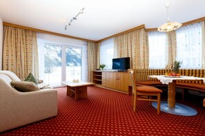 A living room with a sofa, a dining table with a bench, a television, and a red patterned carpet. - Fisherman's dream by the lake (Nesselwängle)