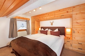 Ein schlafzimmer mit Holzwandverkleidung, einem Bett, einem Kopfteil mit aufgebrachtem Tierkopf und einem Fenster mit Vorhängen.