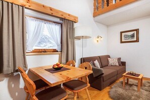 Ein gemütlicher Wohnbereich mit Esstisch aus Holz, braunem Sofa und einem kleinen Beistelltisch.