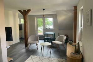 Ett vardagsrum med en tv, två fåtöljer, ett litet bord och ett fönster med utsikt.