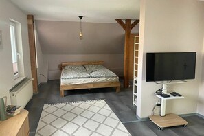 A bedroom with a bed, a TV on a stand, a radiator, and a window. - LEE Anchorage Priepert (Priepert)