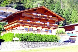 A multi-story wooden building with balconies, surrounded by greenery and a stone wall. - Edelweiss Apartment, Family Wechselberger (Schwendau)