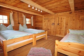 Una cabaña con dos camas de madera, un ventanal con cortinas y un techo de madera con luces colgantes.