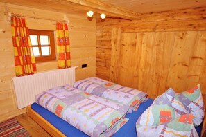 Una habitación tipo cabaña de madera con una cama, cortinas y una ventana.
