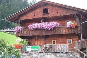 A wooden building with a balcony adorned with flowers, a sign indicating it is a hotel, and a stone staircase leading to the entrance.