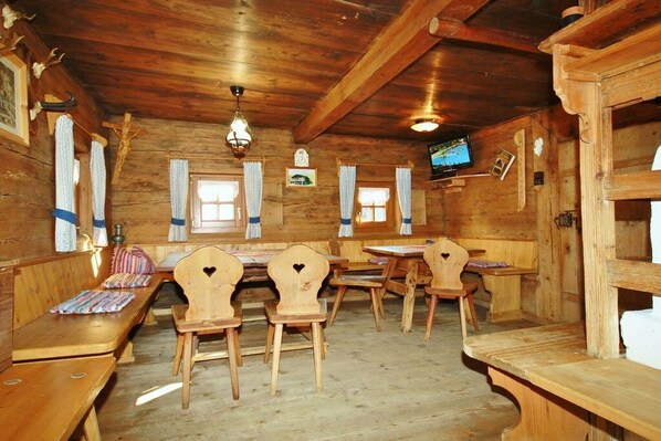 A wooden interior with benches and tables, a television mounted on the wall, and a wooden ceiling.