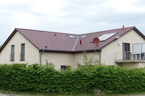 A two-story building with a red-tiled roof, a balcony with a railing, and a green hedge in front. - Holiday home with 2 bedrooms (Göhren-Lebbin)