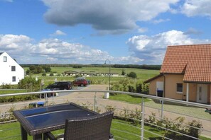 A balcony with a table and chair, overlooking a parking area and a building with a red roof. - Holiday home with 2 bedrooms (Göhren-Lebbin)