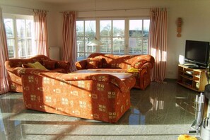 A living room with a sofa set, a television, and a window with curtains. - Holiday home with 1 bedroom (Karnin\/Insel Usedom)