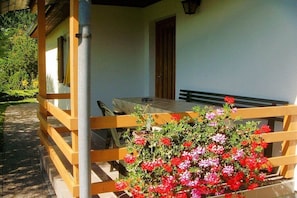 Eine Holzterrasse mit Tisch und Stühlen, einer Bank und einem Blumentopf mit roten und rosa Blüten.