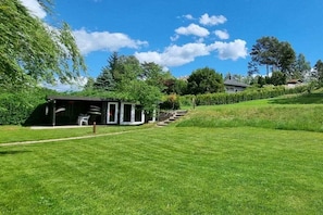 A grassy area with a building that has a covered outdoor seating area and steps leading up to it. - Country house on Lake Priepert (Priepert)