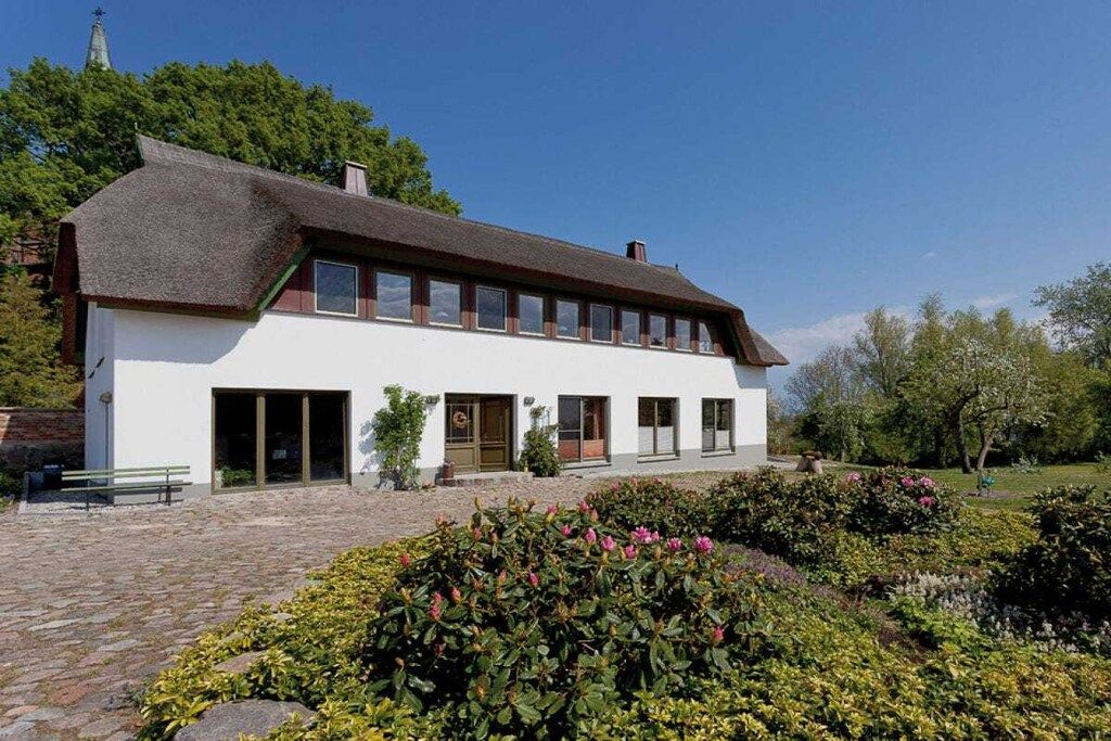 A traditional building with a thatched roof, a central entrance, and a garden with various plants.