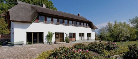 A traditional building with a thatched roof, a central entrance, and a garden with various plants.