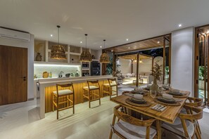 A modern kitchen with a bar area, wooden chairs, and pendant lighting. - Villa Paraiso (Umalas)