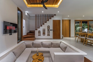Ein modernes Wohnzimmer mit einer Eckcouch, einer Holztreppe und einem Essbereich mit Holztisch und Stühlen.