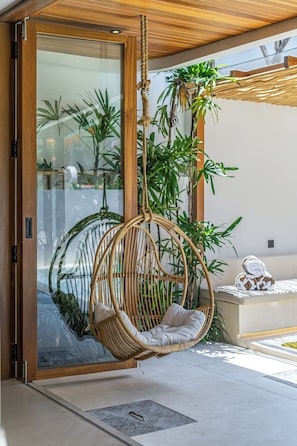 A hanging chair in a modern room with glass doors and a view of greenery outside. - Villa Paraiso (Umalas)