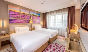 Habitación de hotel con dos camas, un ventanal con cortinas, un televisor de pantalla plana y una pared con varias fotografías enmarcadas.