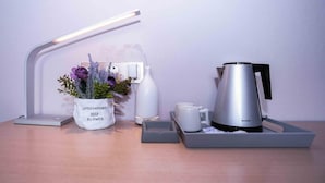 A modern desk setup with a desk lamp, a flower vase, a water bottle, a coffee maker, and two mugs. - Lavande Hotels Harbin Railway Station Zhanqian Square (Harbin)