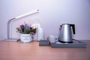 Una moderna configuración de escritorio con una lámpara, un florero, una botella de agua, una cafetera y dos tazas.