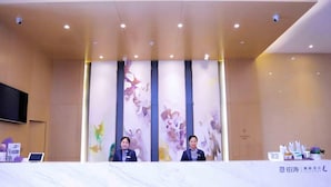 A reception desk with two staff members, a flat-screen TV, and a table with informational brochures. - Lavande Hotels Harbin Railway Station Zhanqian Square (Harbin)