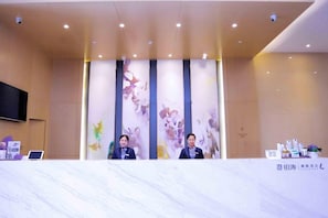 Una recepción con dos empleados, un televisor de pantalla plana y una mesa con folletos informativos.