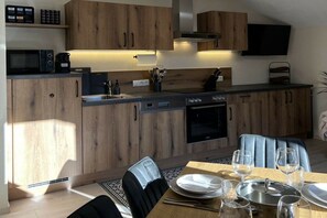 A modern kitchen with wooden cabinets, a built-in microwave, and a dining area with a table set for two. - Apartment "Forest View" (Ried im Zillertal)