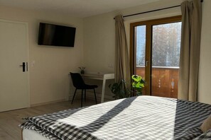 A bedroom with a bed, a desk, a chair, a television, and a window with curtains. - Apartment "Forest View" (Ried im Zillertal)